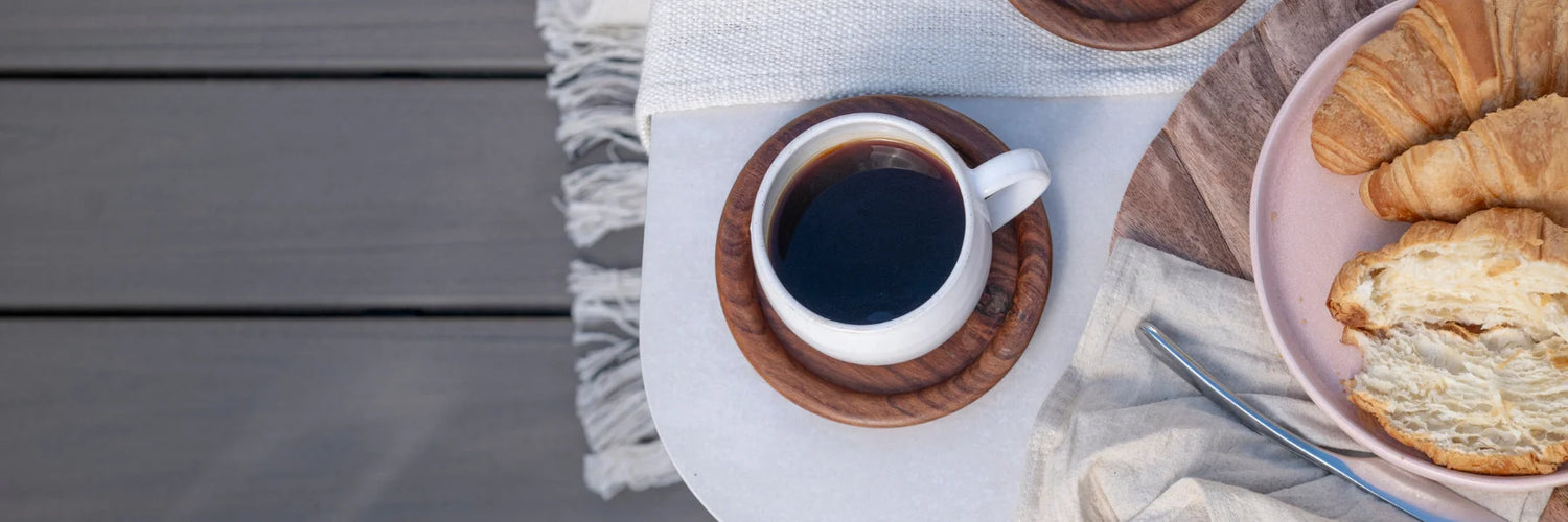 Top-down view of a coffee cup and croissants on a tray resting on Trex Transcend Lineage Biscayne composite deck boards.