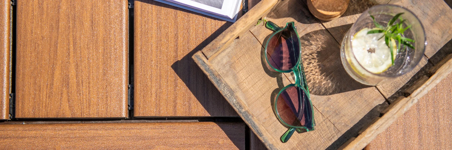 Top-down view of Trex Signature Ocracoke deck boards with a tray holding sunglasses, a book, and a drink with lemon.